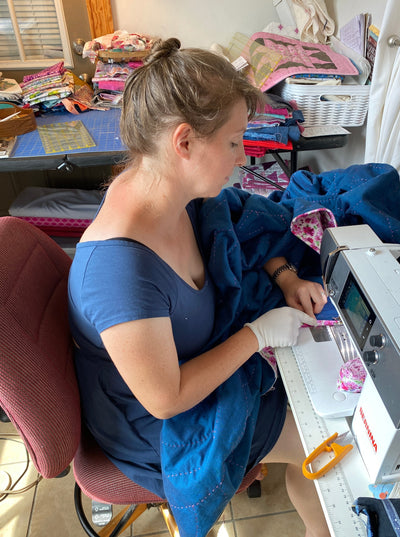 Hope quilt being sewn by Maria Fisher. It is a blue whole cloth quilt with hand quilted magenta arches over the whole quilt. It has a bright magenta flowers with white background.