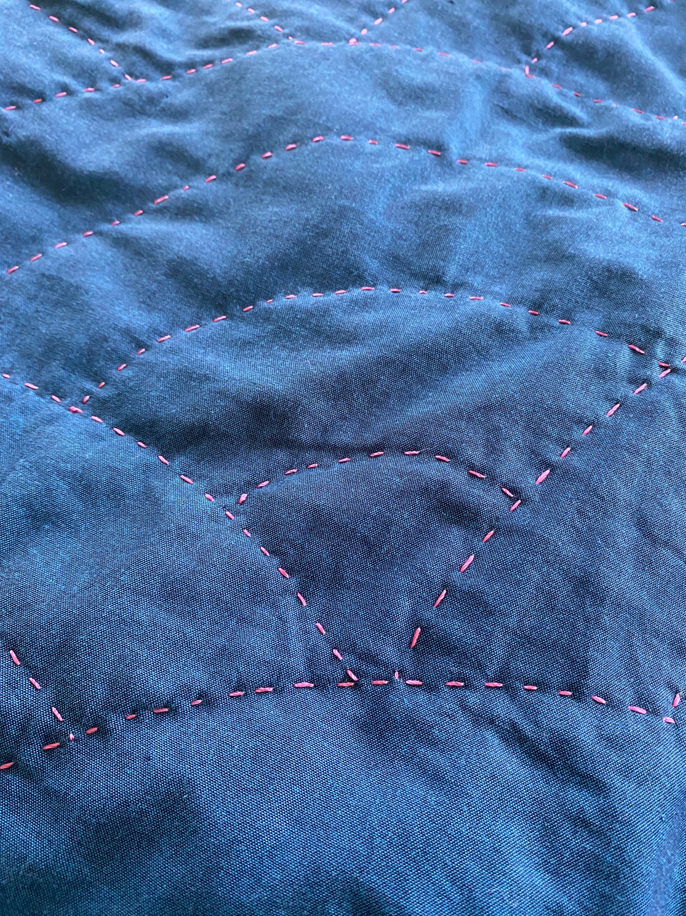 An up-close look at the hand quilting of the magenta thread on the blue whole cloth quilt. 
