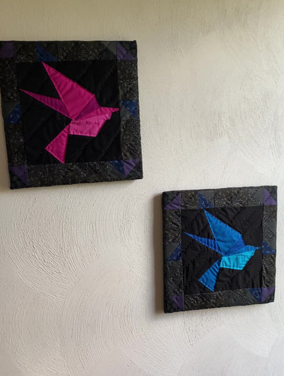 A video for close up details of the hand quilting and Two framed, quilted wall hangings of one blue bird and other of a pink bird. Both have a black background fabric with 1/2 square triangles framing the picture. They are apart of the "Out of darkness" collection.  