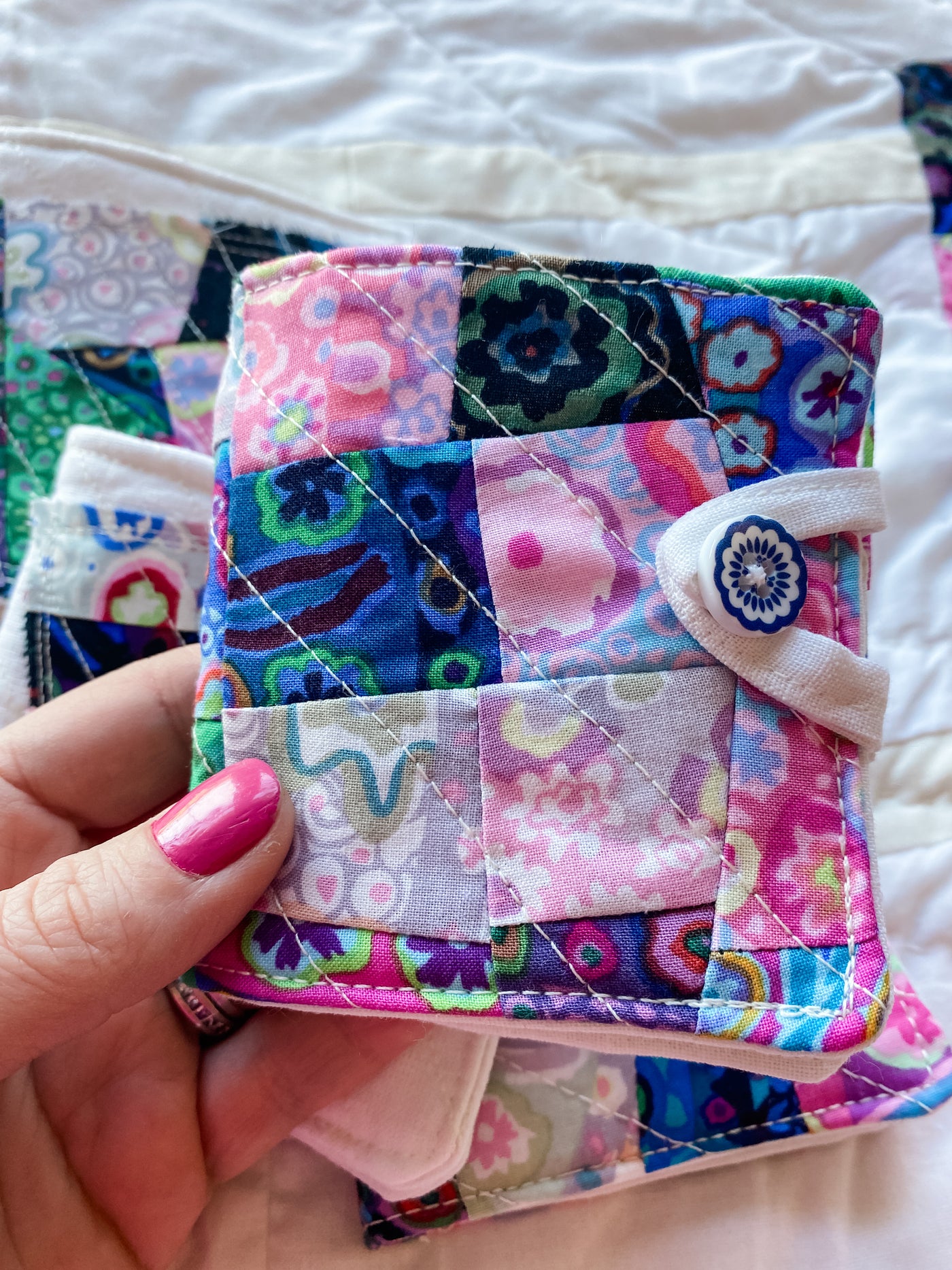 A small quilted 3 1/2" x 3 1/2" needlebook with abstract fabric colors of pinks, blacks, blues. Perfect for needles, thread and scissors