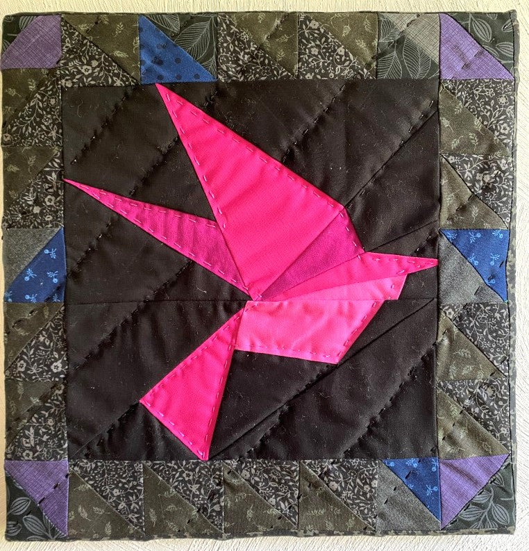 This framed, quilted wall hanging of a pink bird. It has a black background fabric with 1/2 square triangles framing the picture. It is apart of the "Out of darkness" collection. 