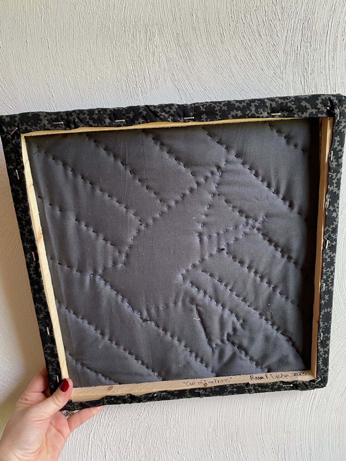 The backside of the framed, quilted wall hanging of the blue bird. It has a black background fabric with 1/2 square triangles framing the picture. It is apart of the "Out of darkness" collection. 