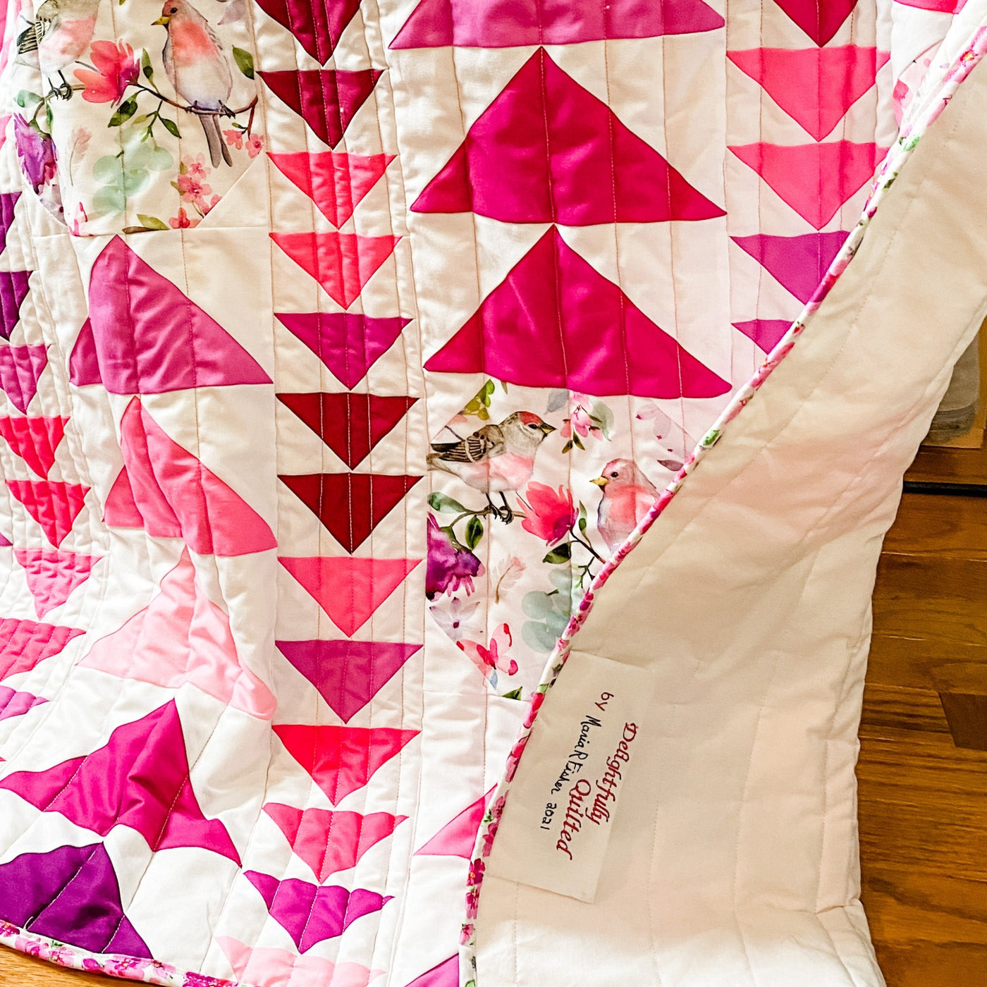 Details of this handmade, heirloom, patchwork of pink and magenta flying geese on a white background with watercolor bird white backing, straight line top quilting, machine top stitched binding, on this sweet lap size quilt