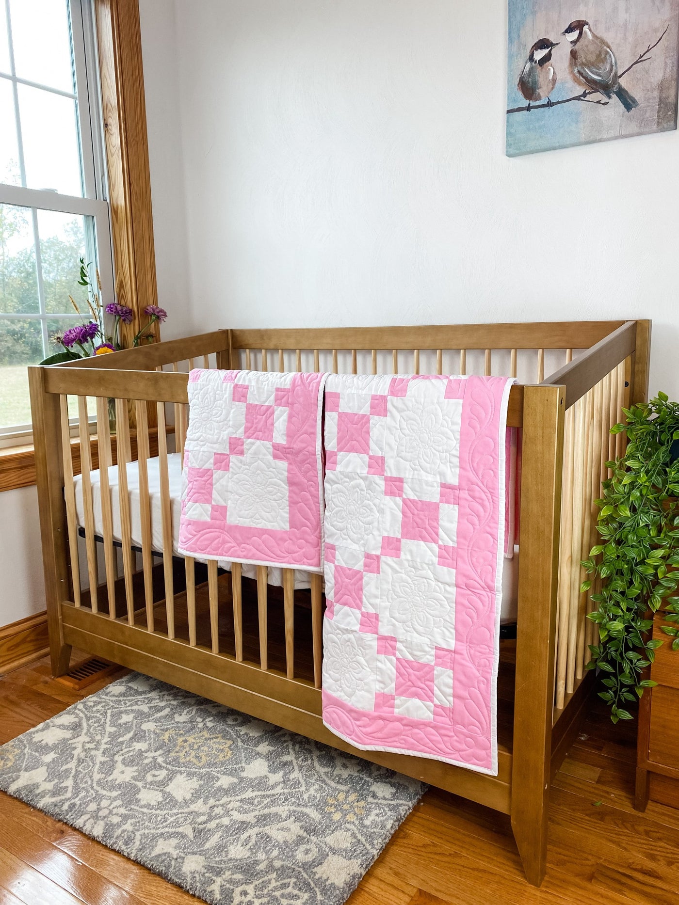 A handmade, heirloom, patchwork of pink nine patch with white background fabric, white backing, 100% cotton batting, Floral top quilting in the white centers, X's in the 9 patch squares, and feathers along the borders, machine top stitched binding, on these baby and crib size quilt