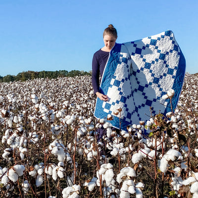 A girl in a field of cotton with a blue and white patchwork quilt