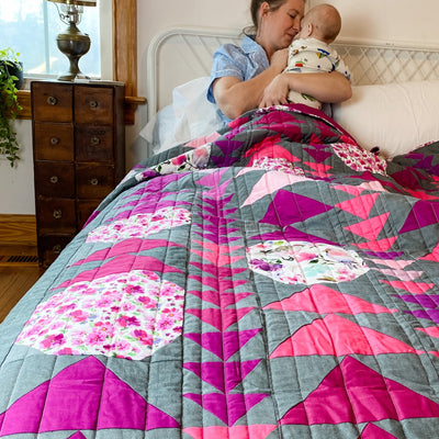 A handmade, heirloom, patchwork of pink and magenta flying geese on a grey/gray background with floral prints, watercolor bird fabric, magenta backing, straight line top quilting, machine top stitched binding, on this sweet queen size quilt