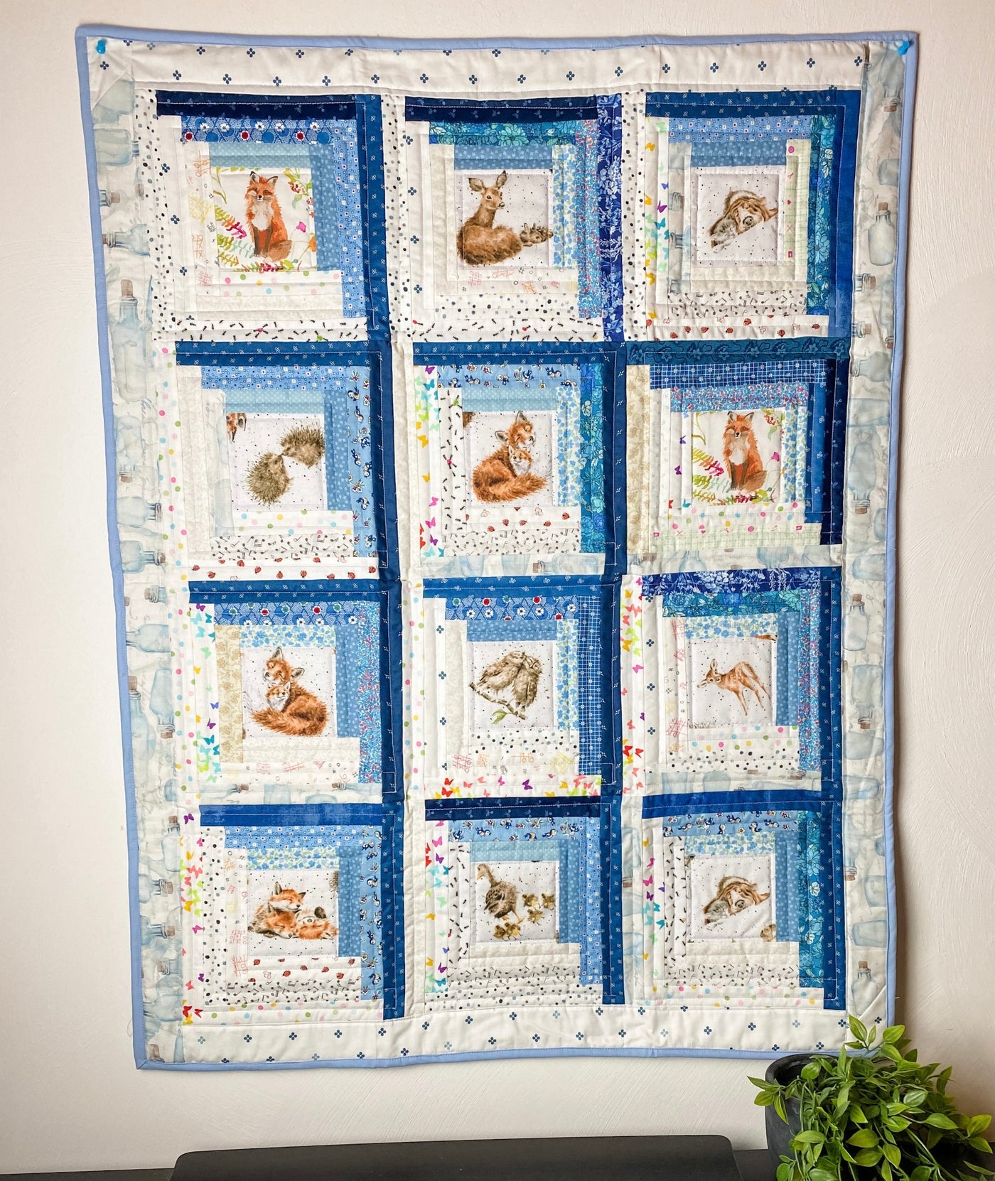 A scrappy or multiple fabrics in blue and white colors  with baby animal print centers. It is a handmade, patchwork, log cabin style crib or baby quilt