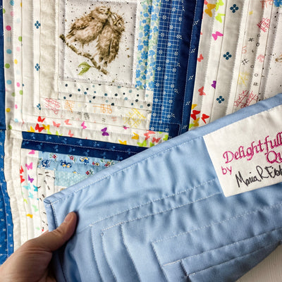 Details of a scrappy or multiple fabrics in blue and white colors  with baby animal print centers. It is a handmade, patchwork, log cabin style crib or baby quilt