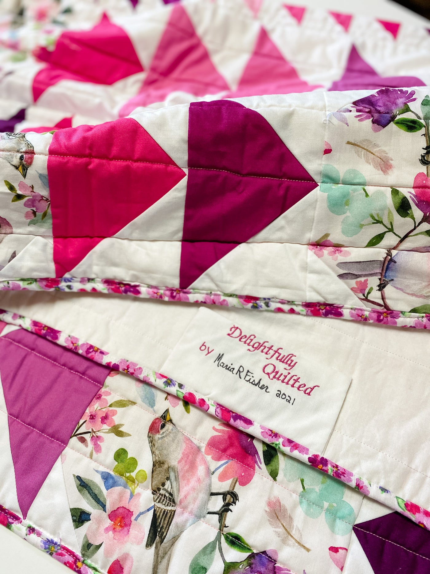 Details of A handmade, heirloom, patchwork of pink and magenta flying geese on a white background with watercolor bird white backing, straight line top quilting, machine top stitched binding, on this sweet lap size quilt