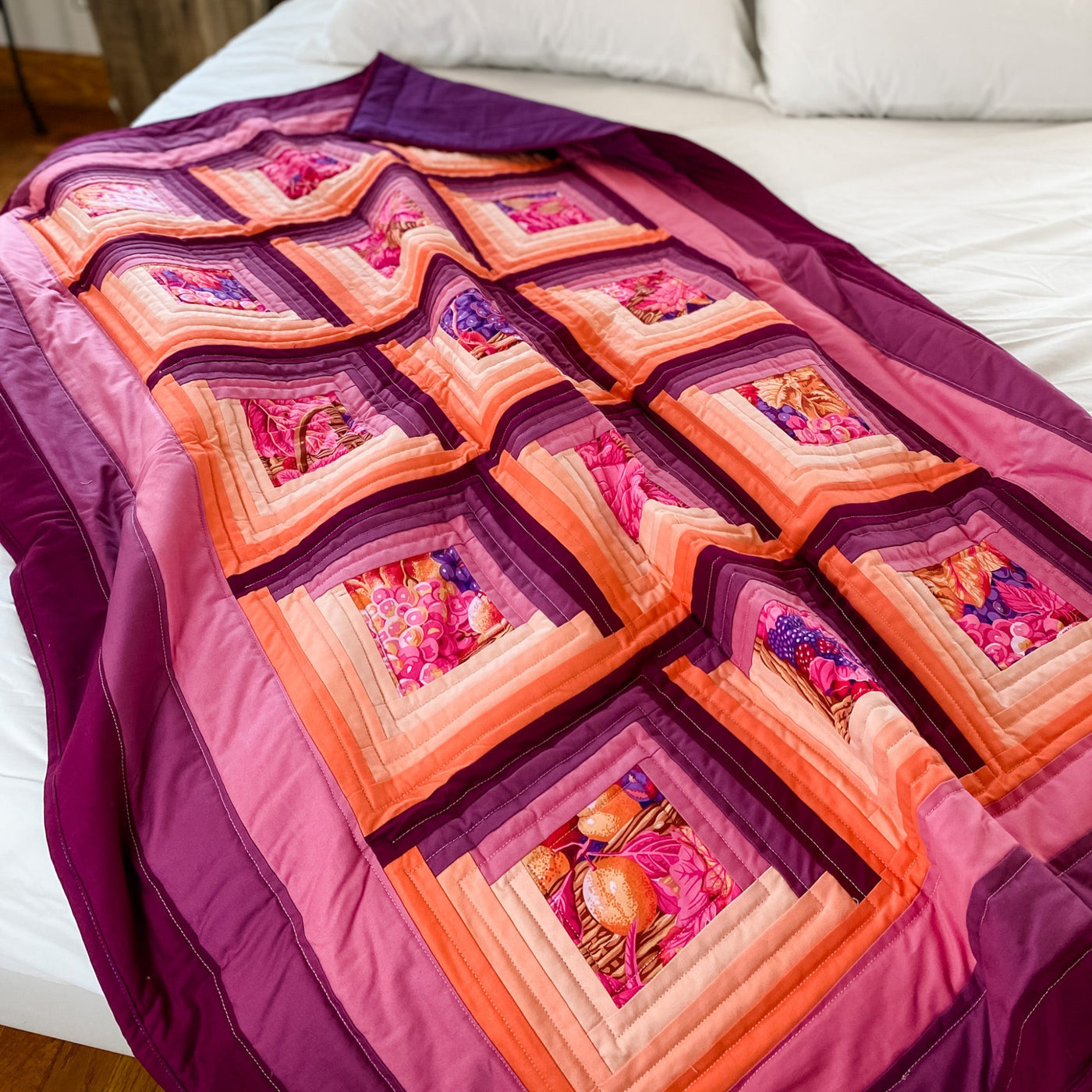 A brightly colored purple and orange colored quilt. It is a handmade, patchwork, log cabin style lap quilt