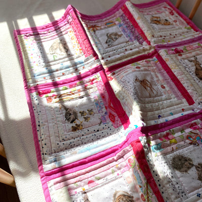 A scrappy or multiple fabrics in pink and white colors  with baby animal print centers. It is a handmade, patchwork, log cabin style crib or baby quilt