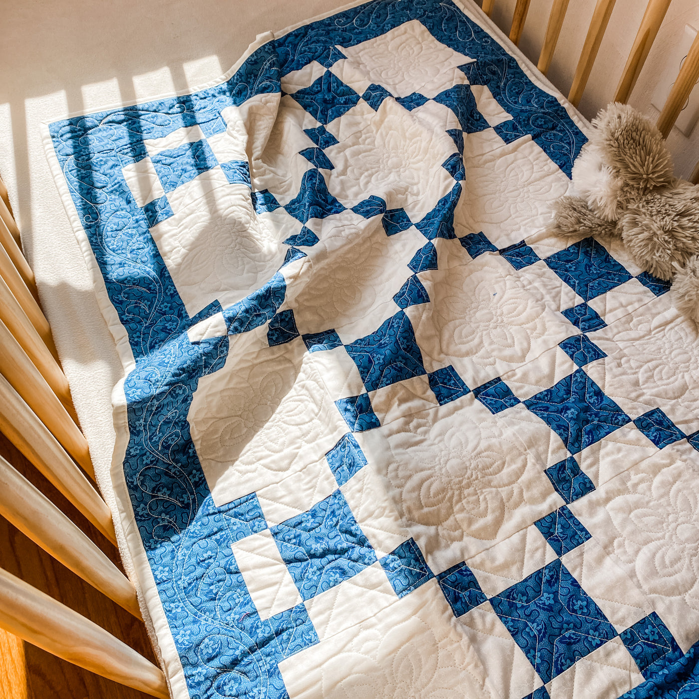  a handmade, heirloom, patchwork of indigo/blue nine patch with white background fabric, natural color backing, 100% cotton batting, Floral top quilting in the white centers, X's in the 9 patch squares, and feathers along the borders, machine top stitched binding, on this crib size quilt