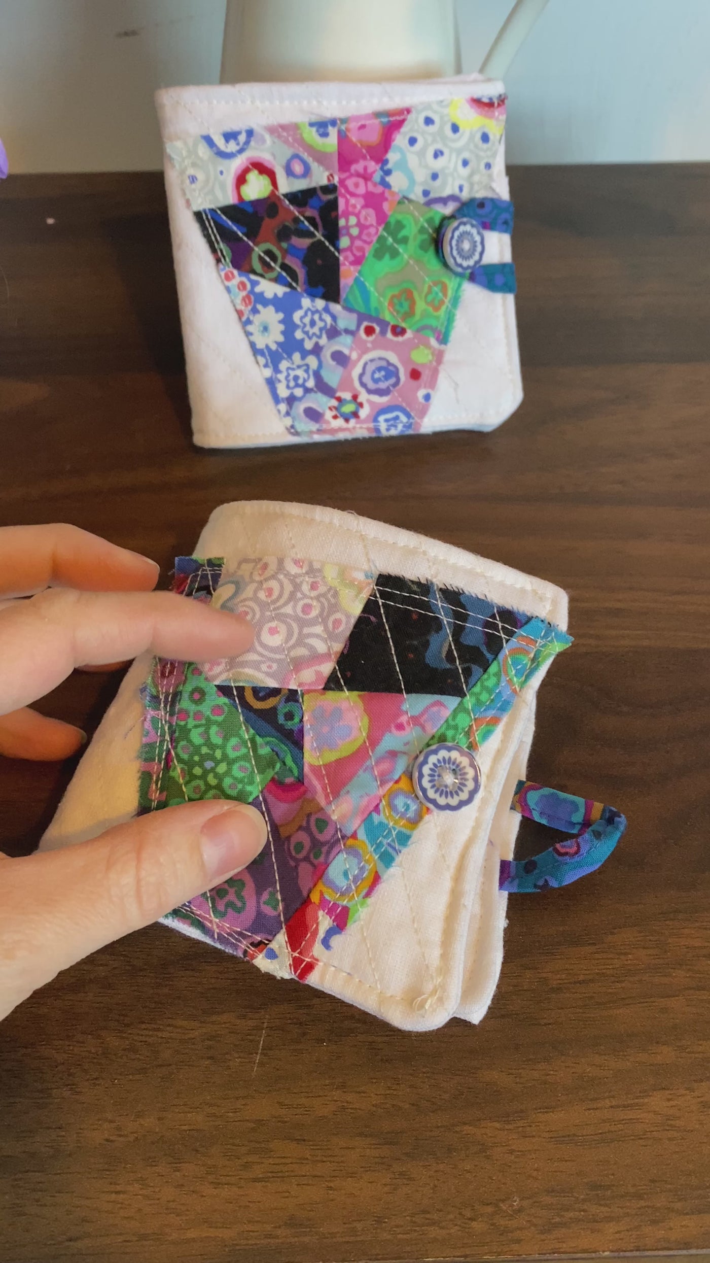 A video of A small quilted 3 1/2" x 3 1/2" needlebook with abstract fabric colors of pinks, blacks, blues. Perfect for needles, thread and scissors